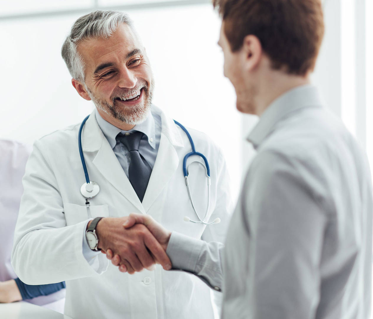 A doctor wearing a lab coat and stethoscope shakes a patient's hand.