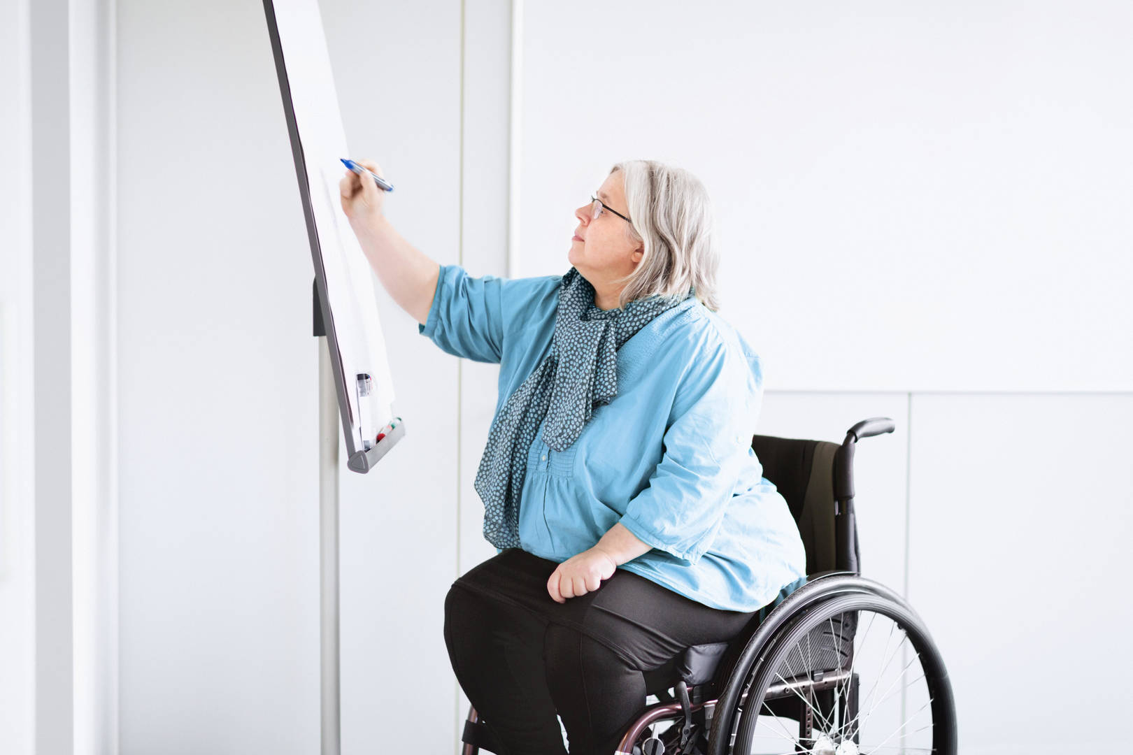 Middle-aged woman in wheelchair draws on a white board