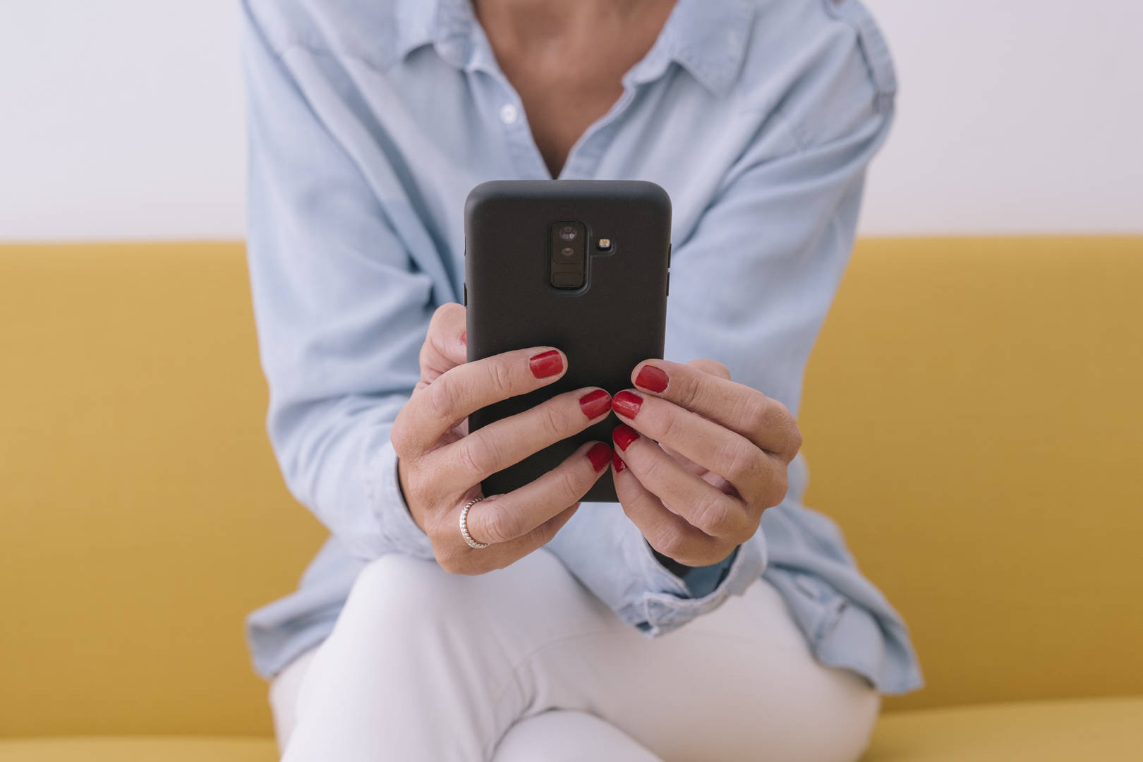 woman using smartphone on yellow couch