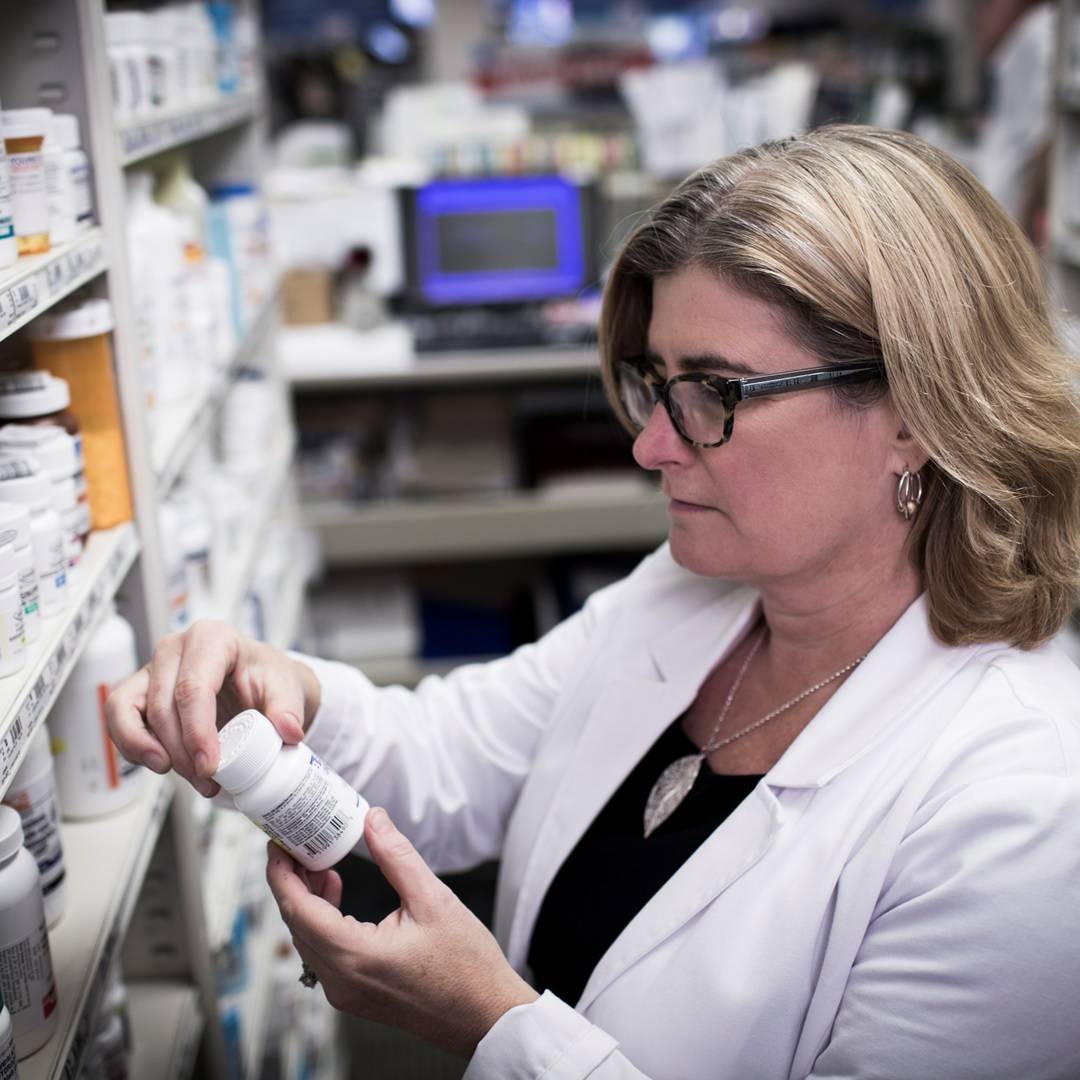 Pharmacist examining a pill bottle behind the pharmacy counter