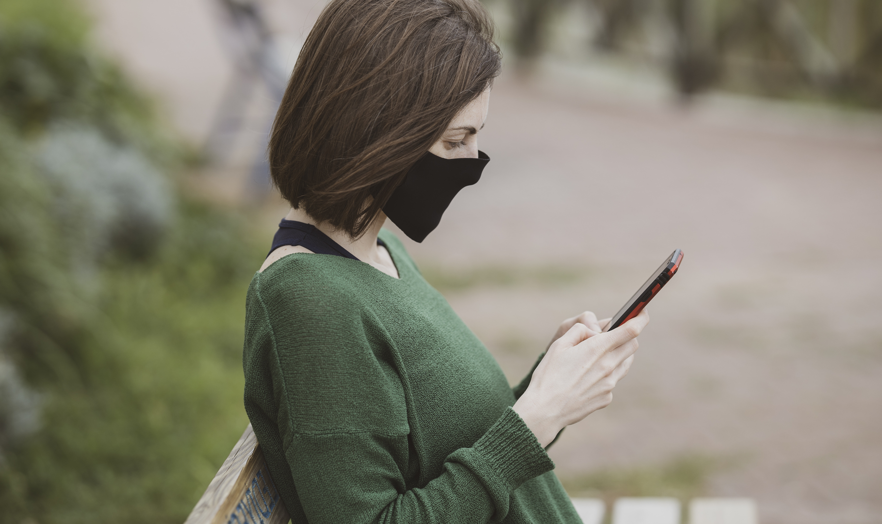 A woman wearing a face mask reading a text message from her pharmacist on her phone