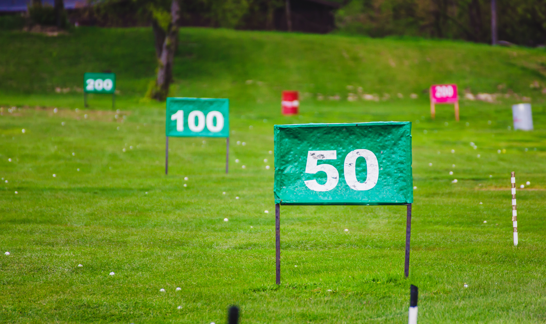 Distance markers laid out on a driving range with golf balls strewn across the grass