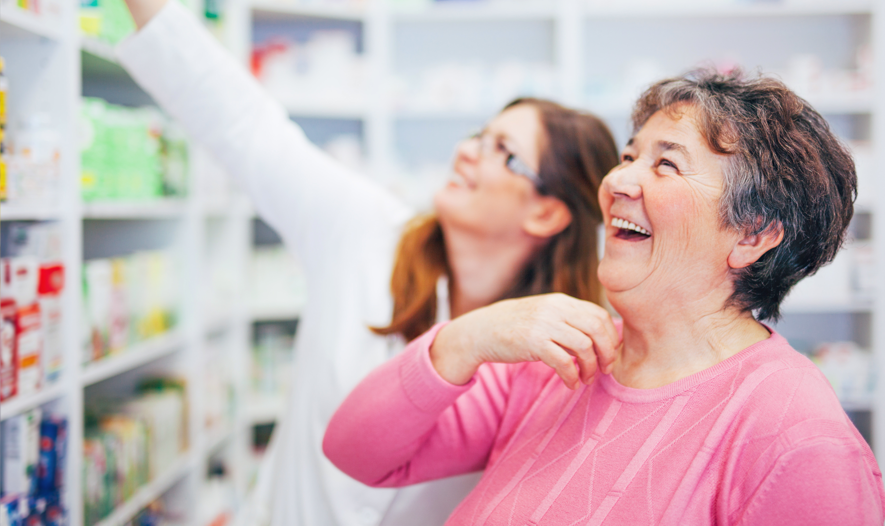 A customer laughing joyfully as a pharmacist helps her find the medication she needs
