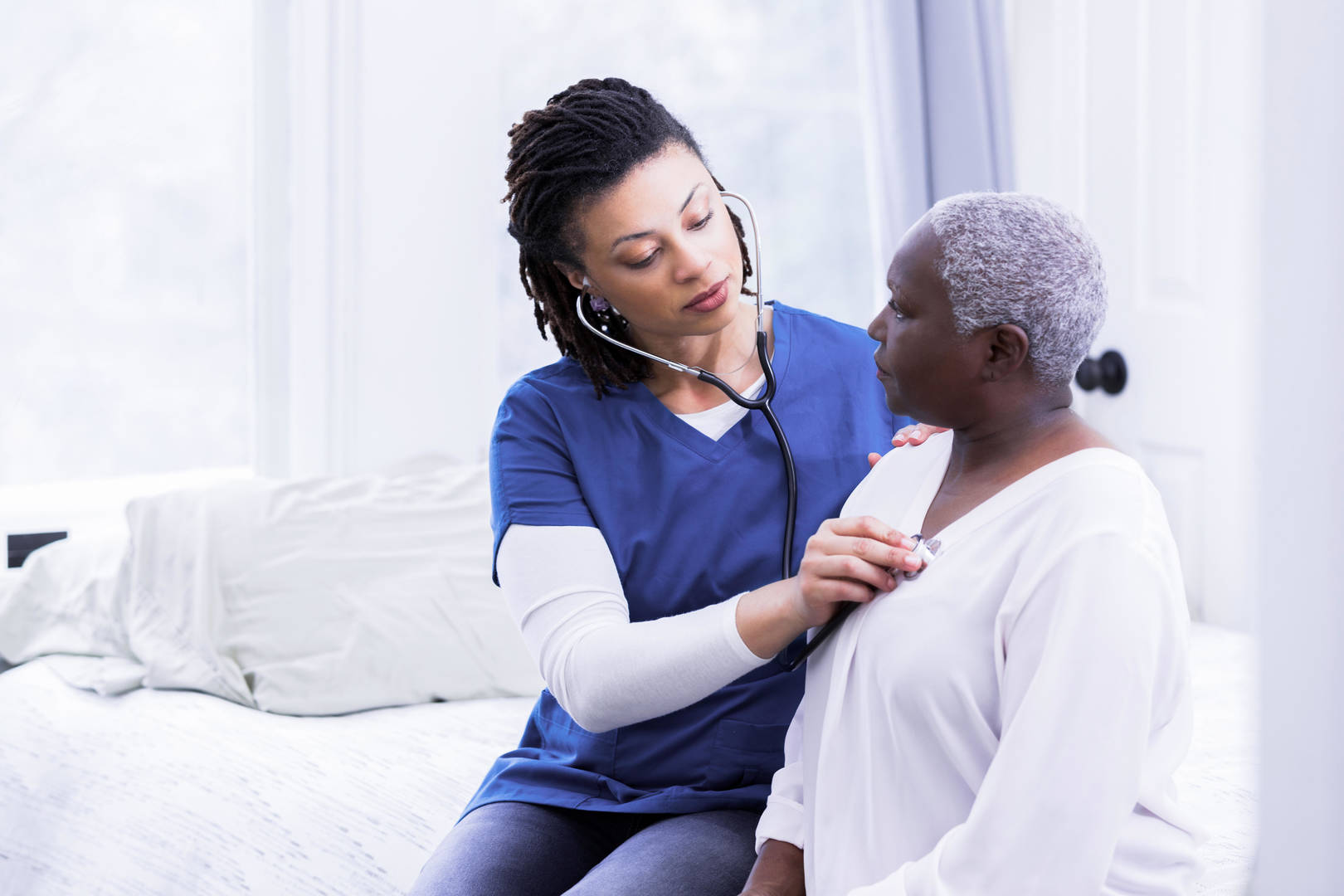 Black female nurse uses stethoscope on older Black female patient