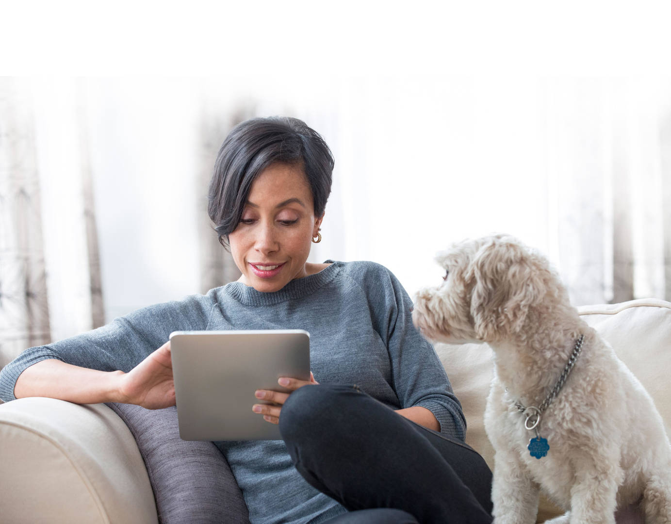Black woman on couch with tablet and dog