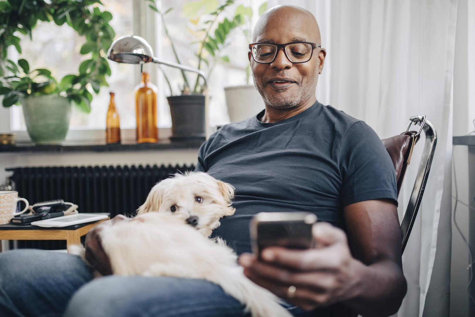Middle-aged Black man looks at smartphone with dog on his lap