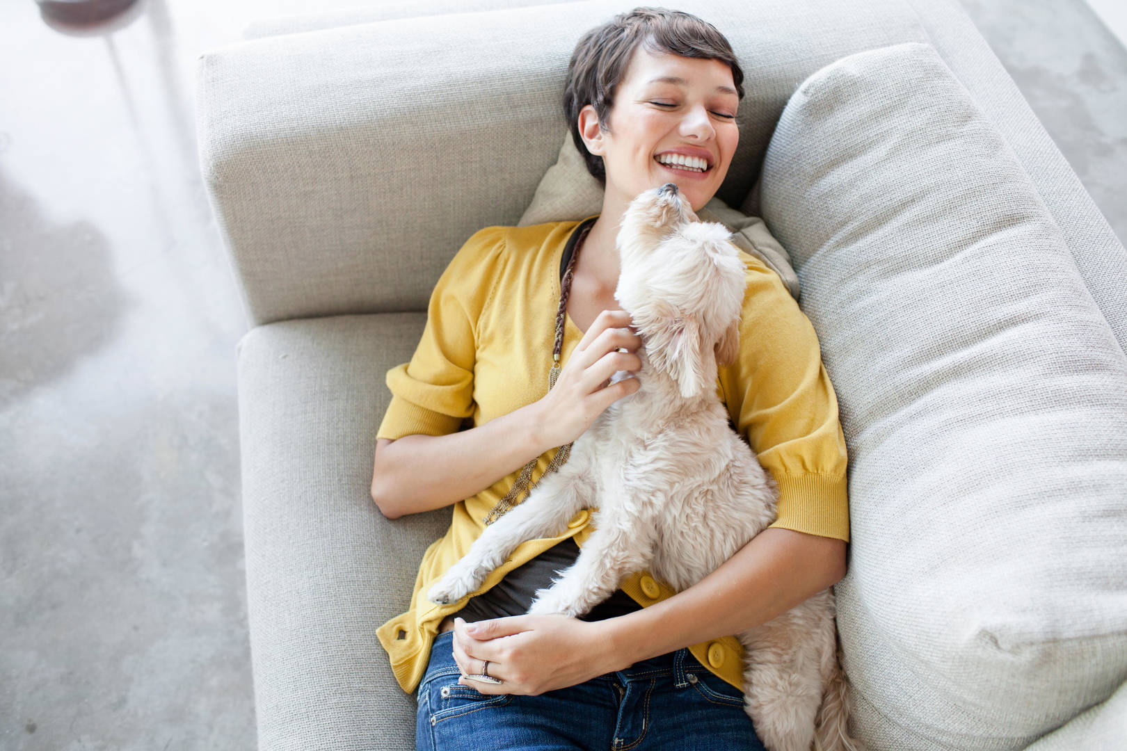 A young woman hugs a white dog while laying on a sofa